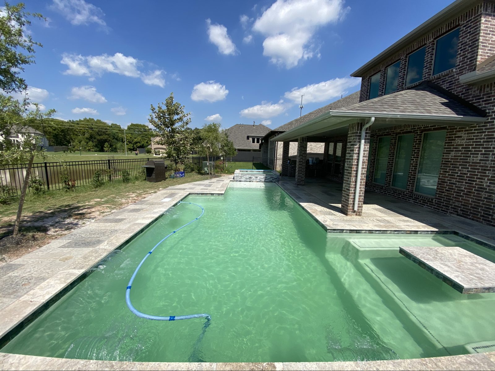Modern rectangular custom Houston pool with tanning ledge, stone pedestal table, and raised stacked-stone spa by Creative Lifestyle Pools